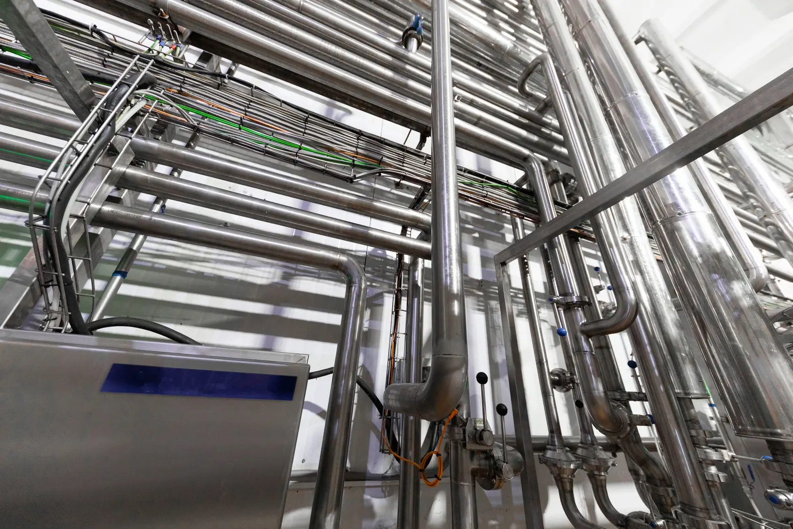 Complex network of shiny stainless steel pipes used in industrial manufacturing processes.